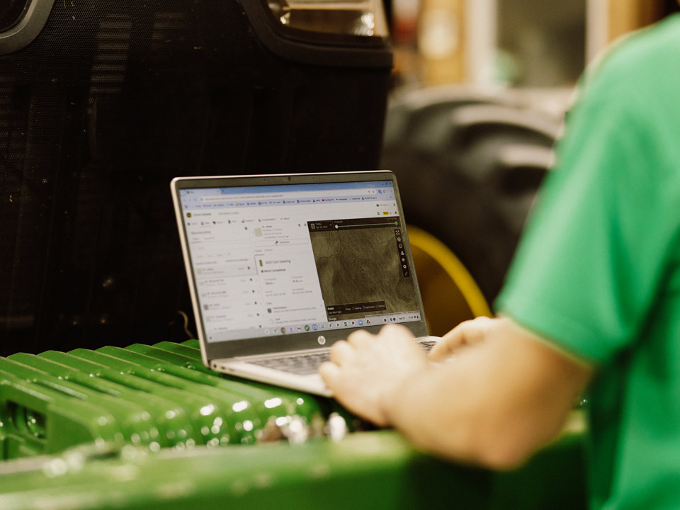 Farmer on laptop behind tractor